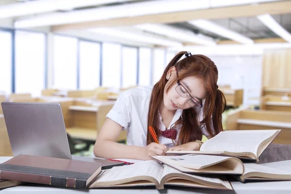 Teenage student writing on the book in class — Stockfoto