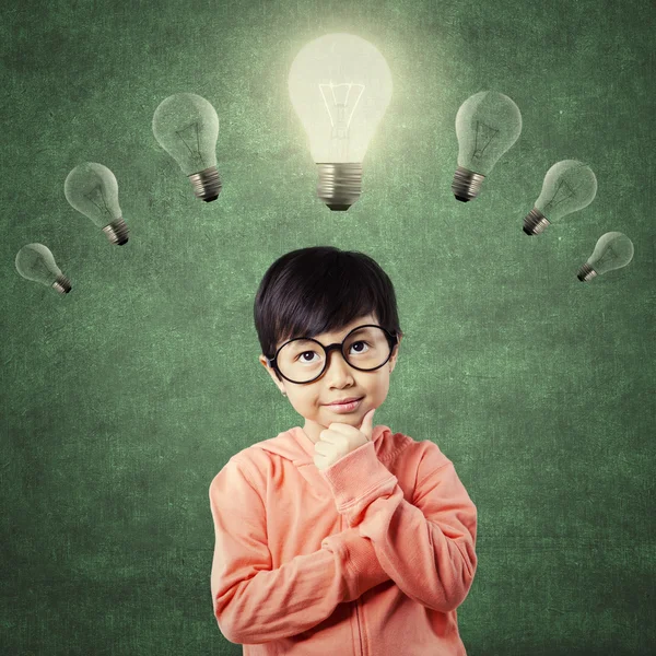 Child in thinking poses under bright light bulb — Stock Photo, Image