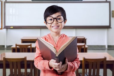 Excited kid with a book in the classroom