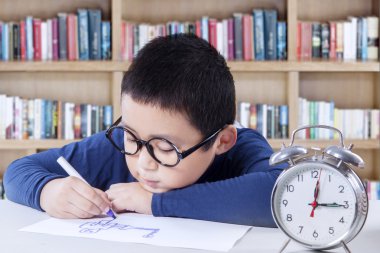 Little boy drawing in library with a clock on desk