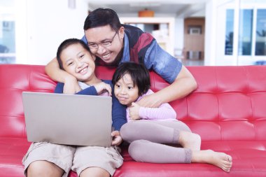 Çok güzel çocuklar kanepede dizüstü kullanarak baba ile