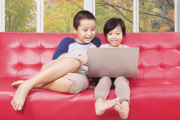 Ragazza carina e suo fratello utilizzando il computer portatile a casa — Foto Stock