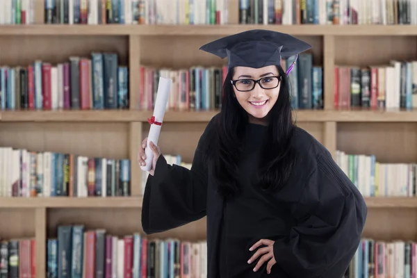Opgewonden afgestudeerde student in jurk poseren in bibliotheek — Stockfoto