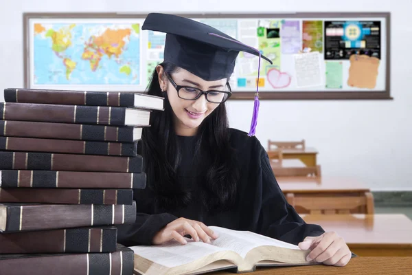 Afgestudeerde student met mortarboard lezen van boeken — Stockfoto