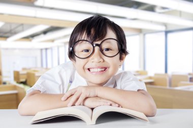 Female kid smiling at the camera while reading book