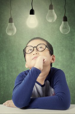 Male primary school student sitting under light bulb