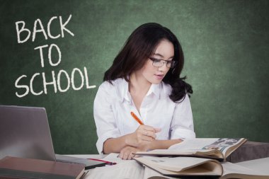 Pretty female student studying with books in class