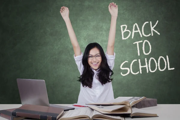 Excited female student raising hands in classroom — Stockfoto