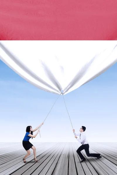 Businesspeople pulling down indonesian flag — 图库照片