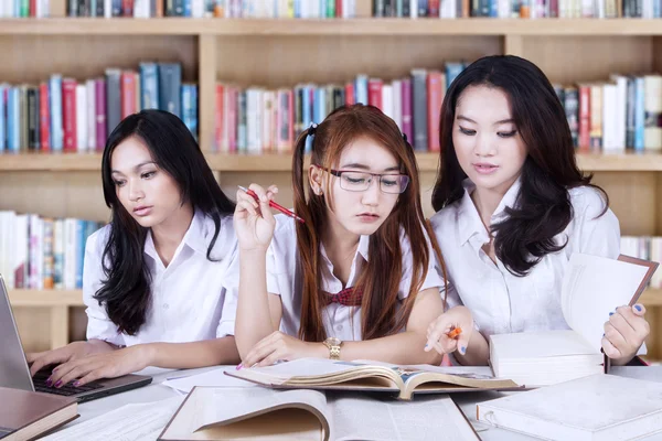 Tres alumnos haciendo tareas escolares en la biblioteca — Foto de Stock