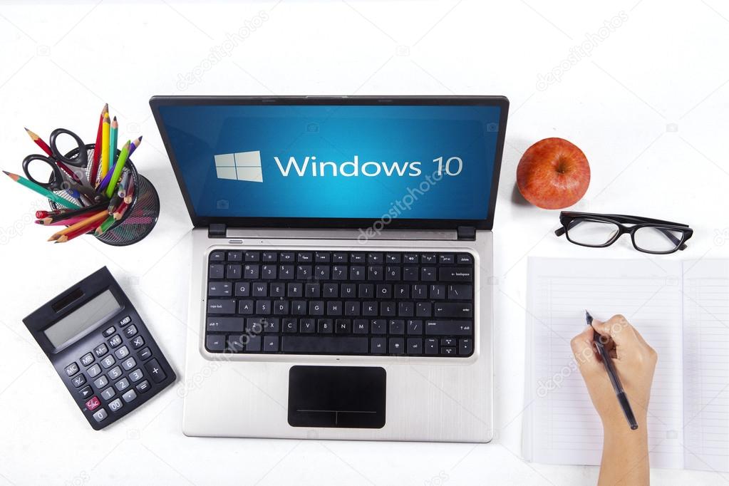 JAKARTA, SEPTEMBER 03, 2015: Closeup of a notebook computer with windows 10 logo and a student hand writing on the book