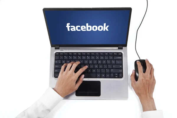 Mani con logo facebook sullo schermo del computer portatile — Foto Stock