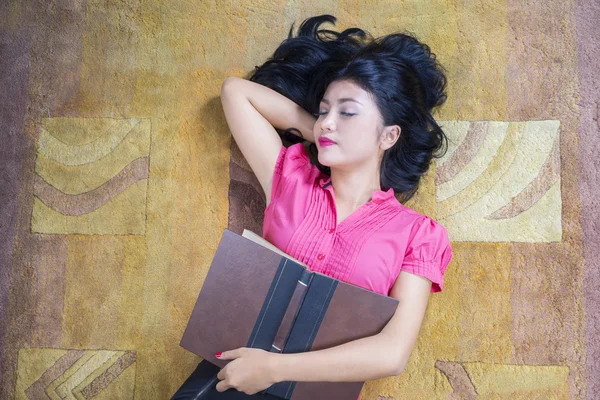 Mujer estudiante sostiene libro y dormir en la alfombra —  Fotos de Stock