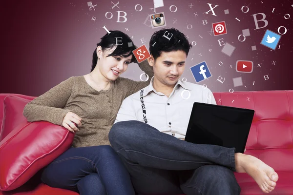 Couple using social network with laptop on sofa — Stok fotoğraf