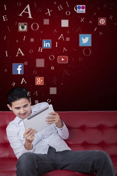 Hombre usando la tableta en el sofá con símbolos de redes sociales —  Fotos de Stock
