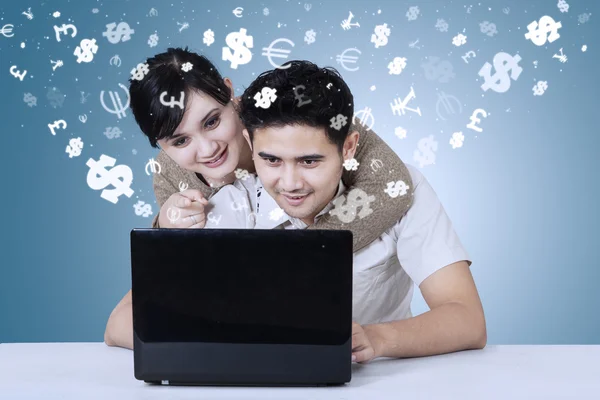 Junges Paar benutzt Laptop mit Währungssymbolen — Stockfoto