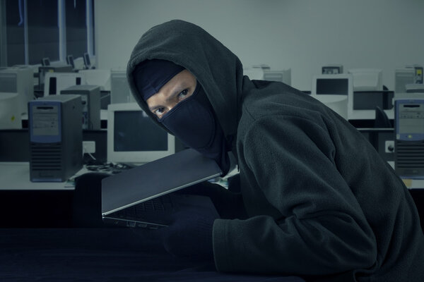Villain with balaclava stealing laptop in the office