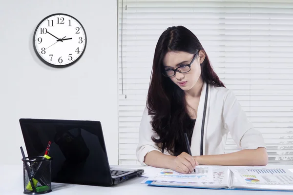 Frau arbeitet im Büro mit Uhr an der Wand — Stockfoto