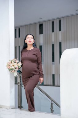 Modern İç Merdiven Üzerinde Kahverengi Elbiseli Asyalı Zarif Kadın Çiçekleri Tutuyor