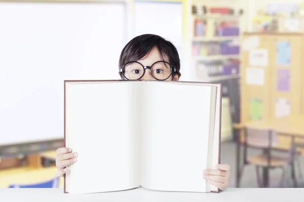 Pequeno estudante mantém livro vazio em sala de aula — Fotografia de Stock