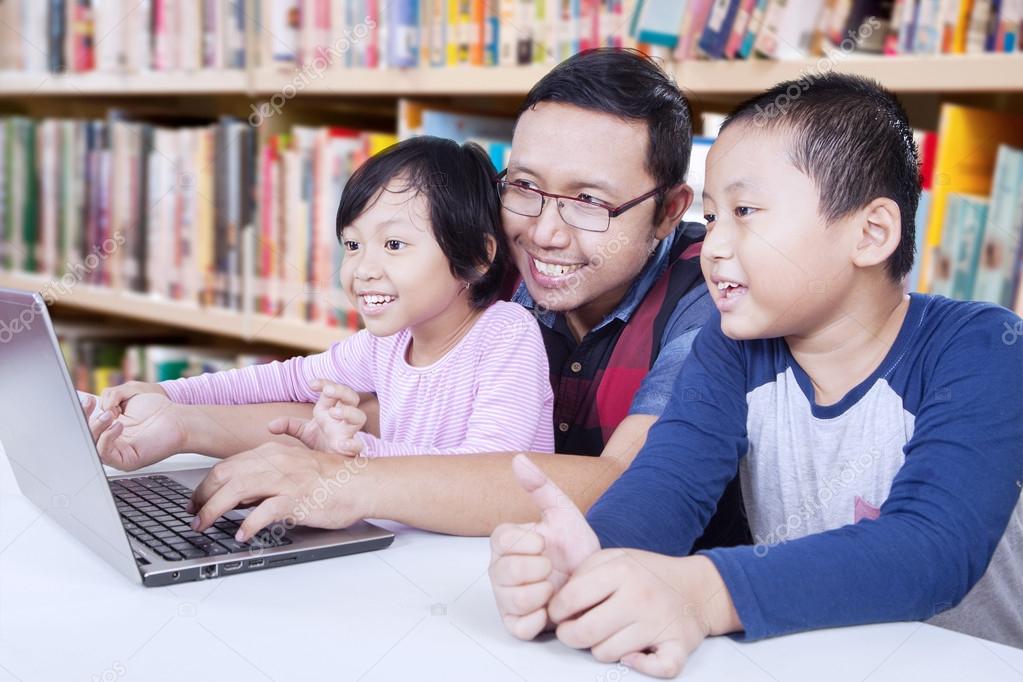 Two children using laptop with teacher in library