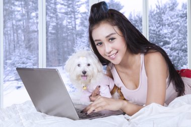 Happy woman and her puppy using laptop on bed