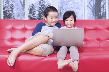 İki çocuk kanepede dizüstü bilgisayar kullanarak