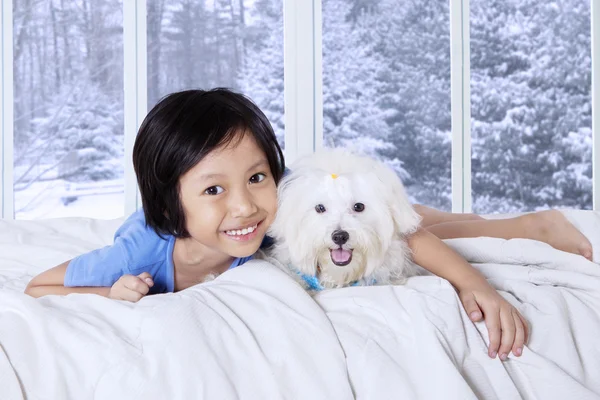 Little girl lying on bed with her puppy — Stock Fotó