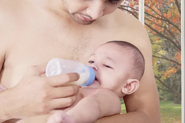 Male baby drinking milk with his father — Stockfoto