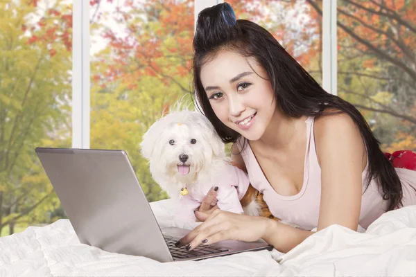 Mujer bonita usando el ordenador portátil con cachorro en la cama — Foto de Stock