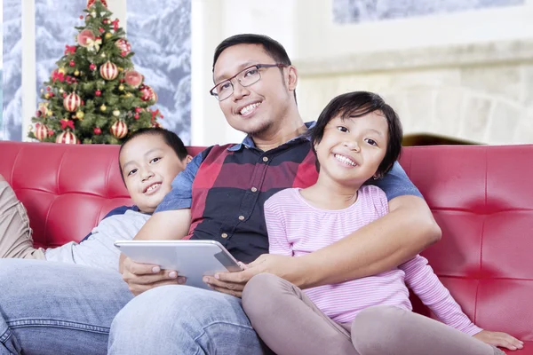 Två barn och pappa med tablett ler mot kameran — Stockfoto