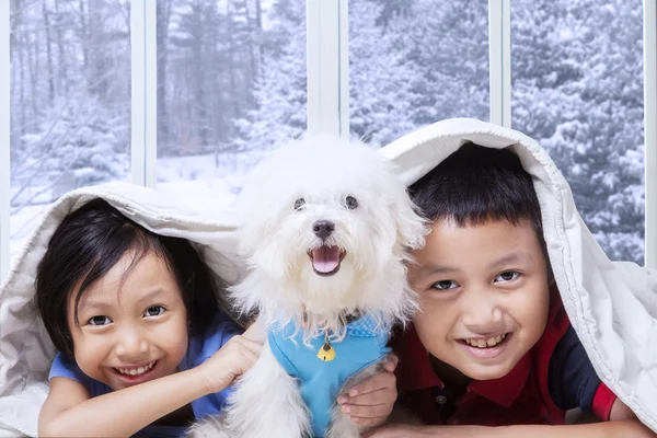 Deux enfants et leur chiot couchés sous la couverture — Photo