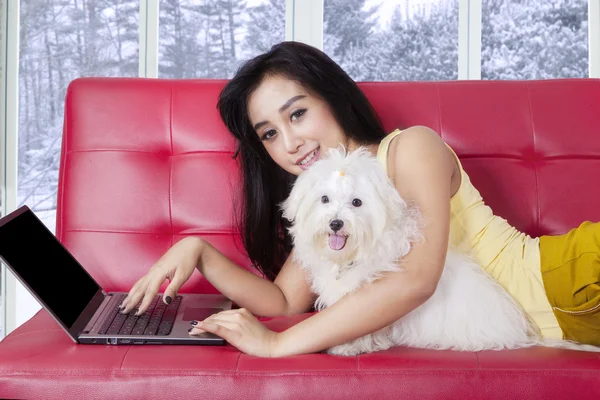 Жінка використовує ноутбук на дивані зі своєю собакою — стокове фото