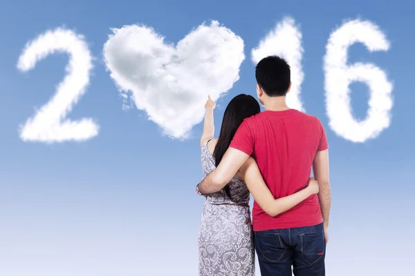 Pareja joven apuntando a los números en forma de nubes 2016 — Foto de Stock