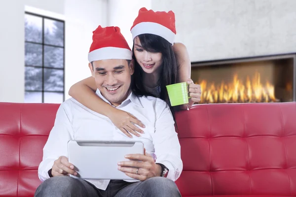 Para z Boże Narodzenie kapelusz za pomocą tabletu na kanapie — Zdjęcie stockowe