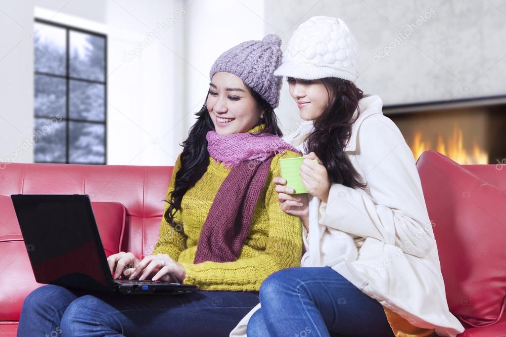 Two women with winter clothes using laptop