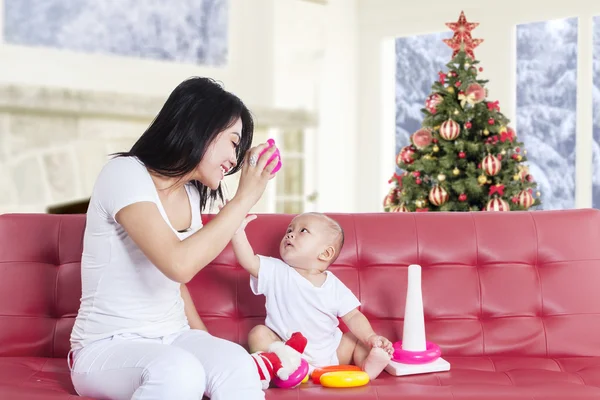 Mother and baby playing on sofa with christmas tree — Stock Photo, Image