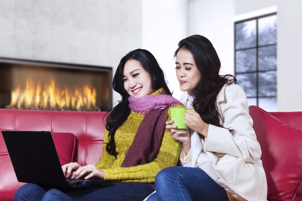 Two girls with winter clothes using laptop at home — Stock Photo, Image