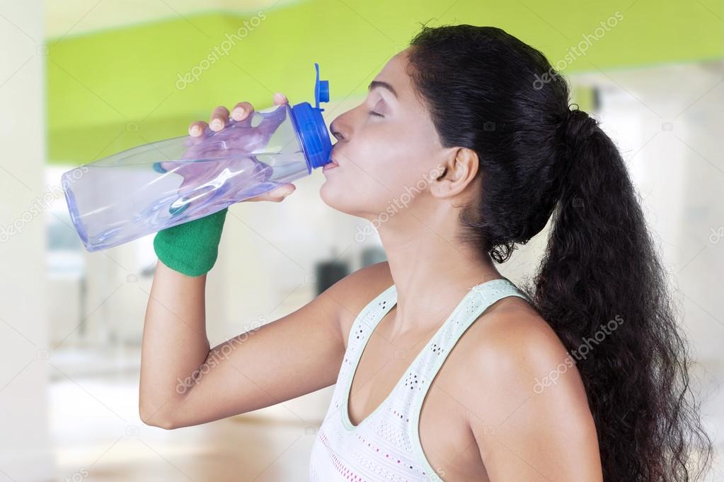 Indian woman drinks water in fitness center