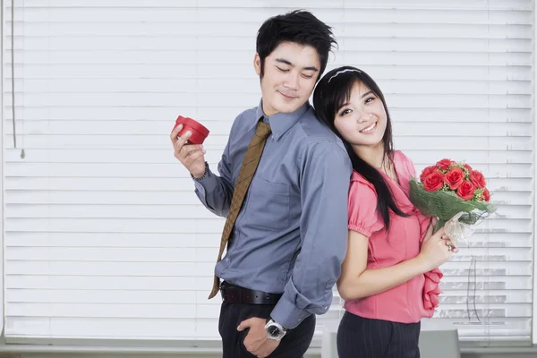 Atractiva pareja sosteniendo un regalo y flores — Foto de Stock