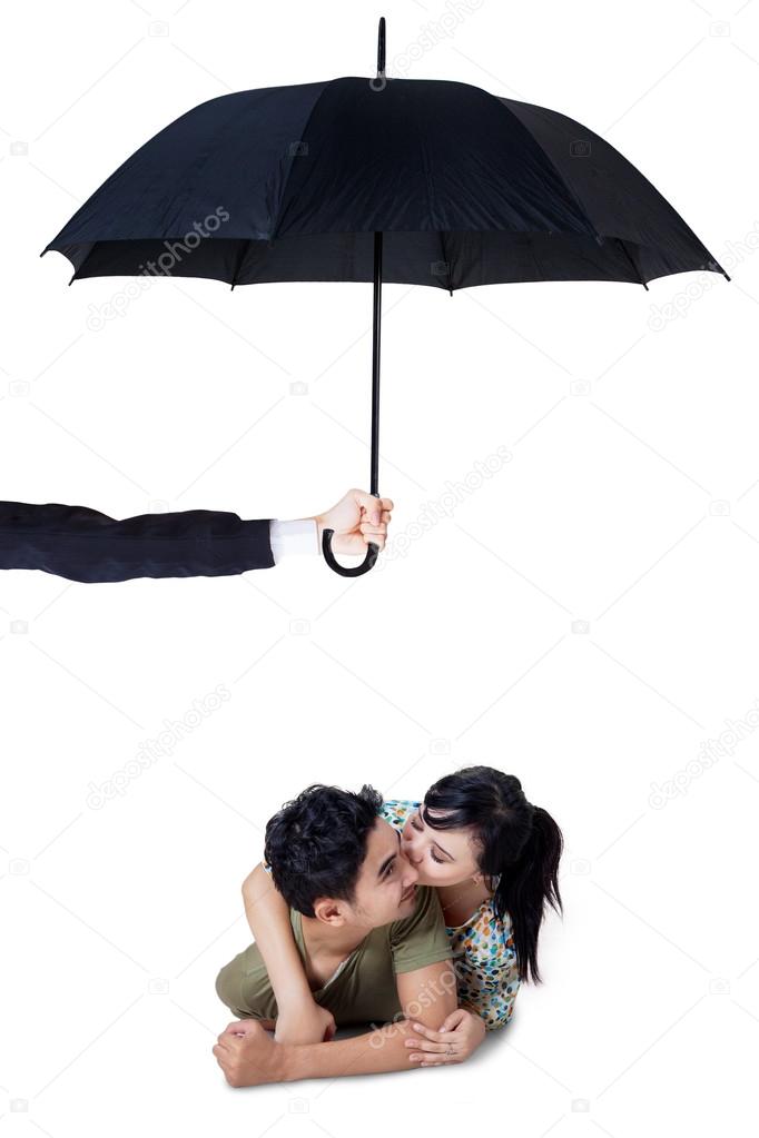 Happy couple kissing in studio under umbrella