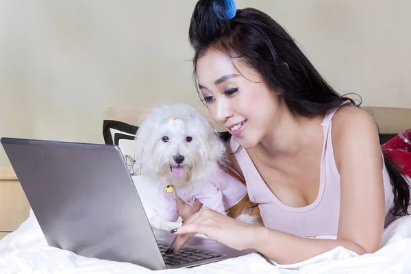 Kvinna och hund spelar laptop på sängen — Stockfoto