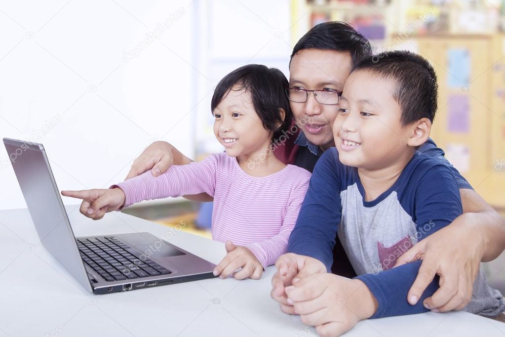 Two children using laptop with teacher in class
