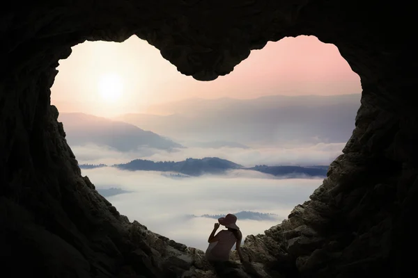 Mulher sentada dentro da caverna e desfrutar de vista montanha — Fotografia de Stock