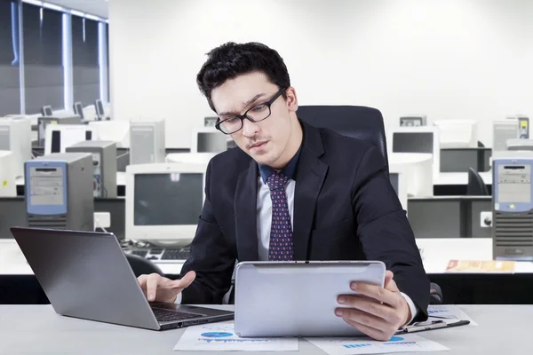 Hombre trabajando en el ordenador portátil mientras mira la tableta —  Fotos de Stock