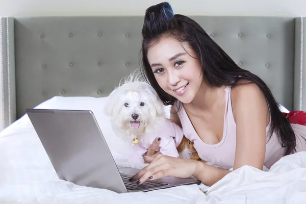 Modelo feminino usa notebook com cão na cama — Fotografia de Stock
