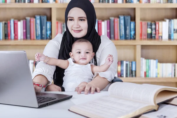 Moeder en baby via laptop in bibliotheek — Stockfoto