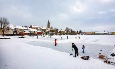 Telc, Çek Cumhuriyeti - 16.1.2021: Babaları olan çocuklar Telc kentindeki doğa su havuzunda buz hokeyi oynuyorlar. Kar yağarken kışın.