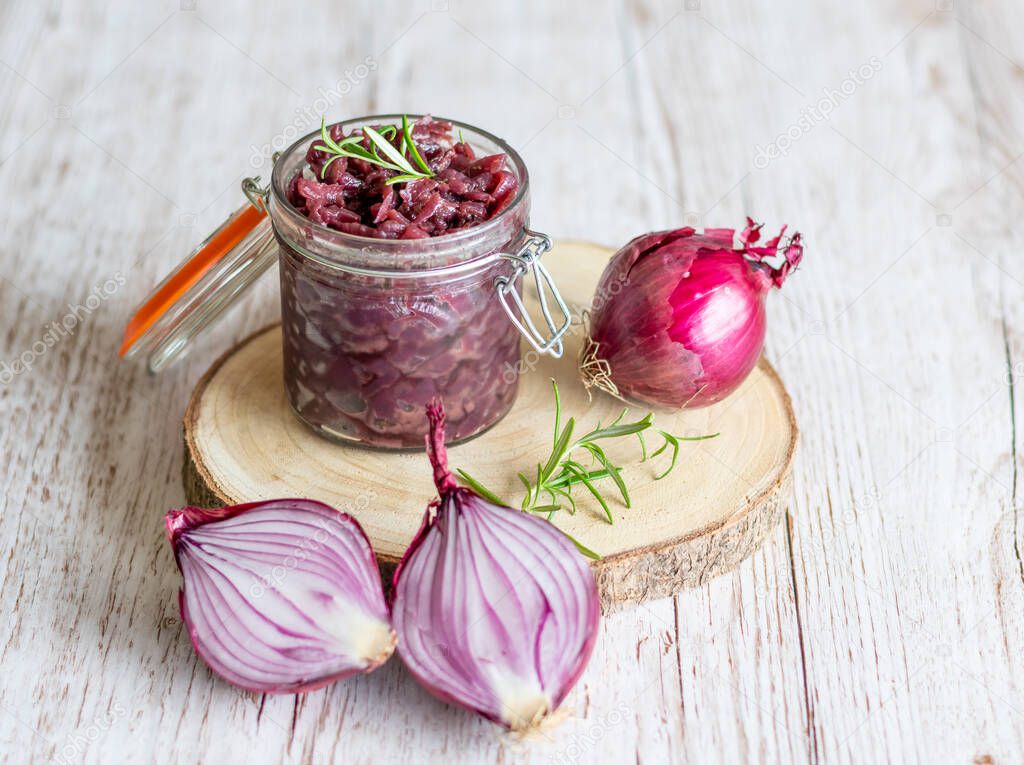 Red onion marmalade placed on wooden trunk with wood texture background. Jam from onion is delicious part of French cuisine. Homemade jam in transparent glass, vibrant colors, soft light.