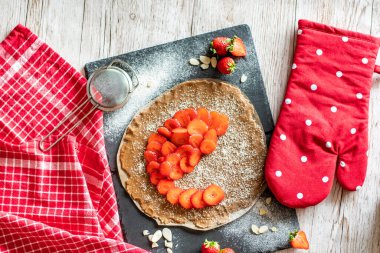 Çilekli ve bademli ev yapımı turtalı kek, siyah masa ve ahşap masa. Yanında yemek aletleri olan kırmızı havlu.